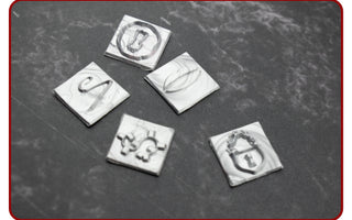 Close-up of engraved square brass wax stamp dies on a dark surface