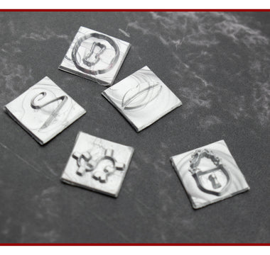 Close-up of engraved square brass wax stamp dies on a dark surface