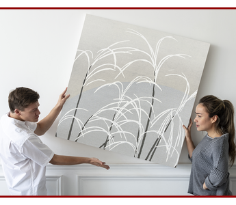 Two people hanging a large canvas print on an interior wall